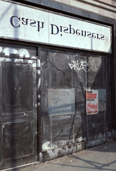 Boarded-up shopfront, 'Cash Dispenser' sign reversed
